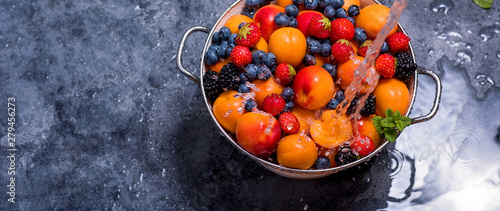 Fototapeta Naklejka Na Ścianę i Meble -  Water splashing on fresh summer fruits and berries, apricots, blueberries, strawberries in colander, washing fruits and berries, vegan healthy food