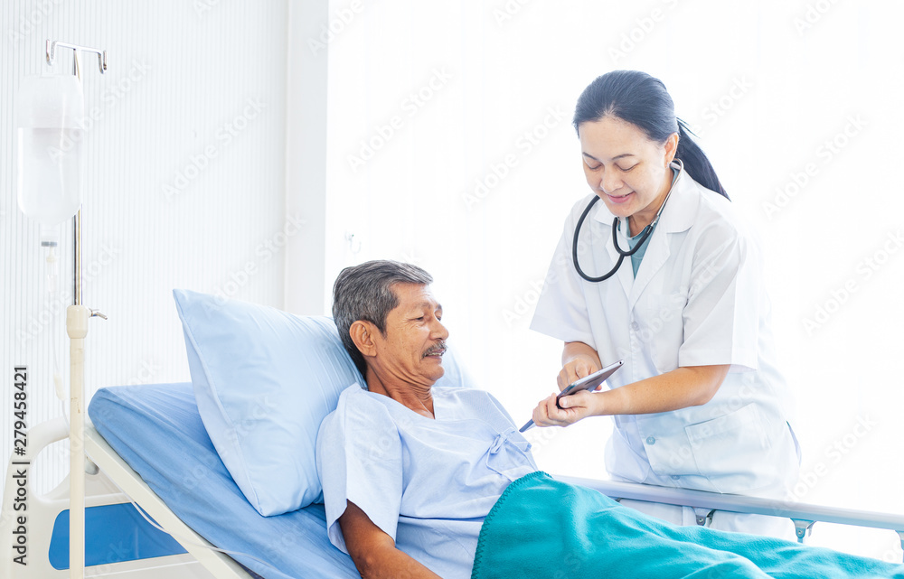 Fototapeta premium Asian woman professional doctor with clipboard visiting, talking, and diagnosing the old man patient lying in patient’s bed at hospital ward