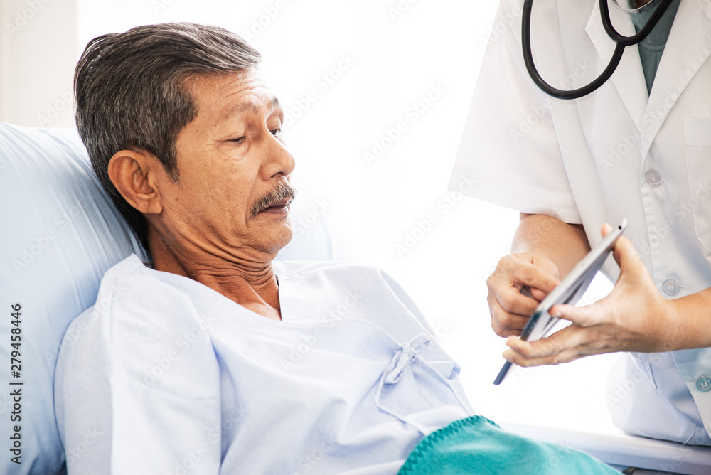 Asian woman professional doctor with clipboard visiting, talking, and diagnosing the old man patient lying in patient’s bed at hospital ward Asian woman professional doctor with clipboard visiting, talking, and diagnosing the old man patient lying in patient’s bed at hospital ward