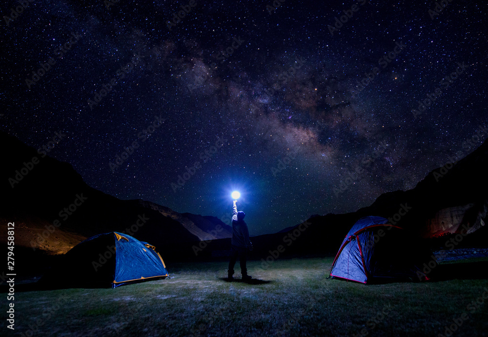Silhouette of climber standing against the Milky Way with a flashlight in his hands. camping under the milkyway