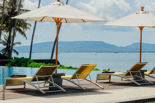 Beautiful tropical swimming pool in  hotel or resort with umbrella, coconuts tree sun-loungers, palm trees with infinity pool view, ocean and mountain background. photo