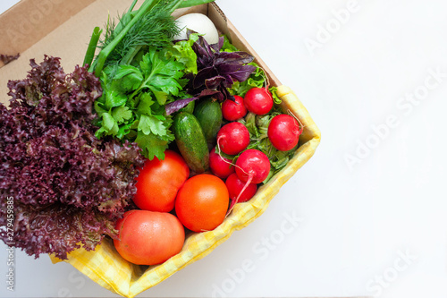 fresh cucumbers, tomatoes, radishes, lettuce, basil, parsley in a box with a yellow napkin. space for text