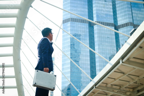 An Asian businessman holding a bag looking up at a tall building. Have space to write text