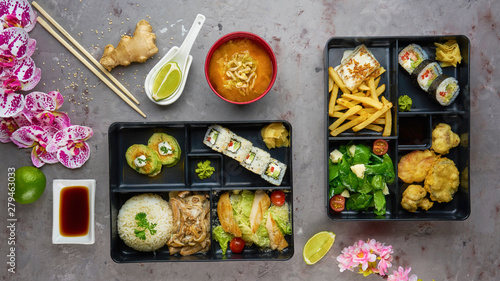 Japanese cuisine. lunch box set, sushi roll, salad, miso, chicken, sauce and wasabi on grey background.