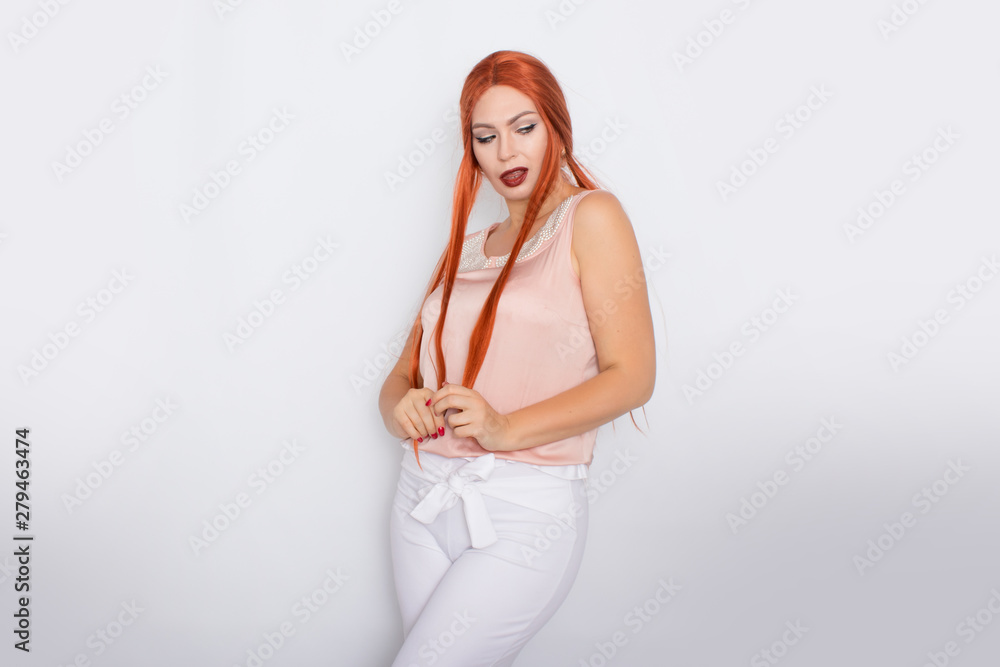 Studio portrait of a red-haired woman with long hair. Business clothes - white pants and light pink blouse with pearls Studio portrait of a red-haired woman with long hair. Business clothes - white pants and light pink blouse with pearls