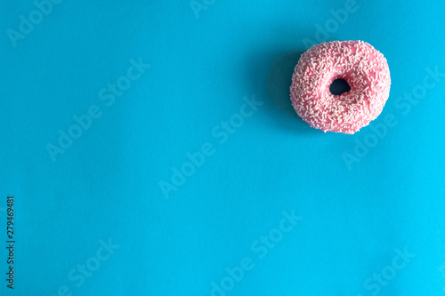 Fresh tasty donut in icing and sprinkling on the right on a blue background. View from above