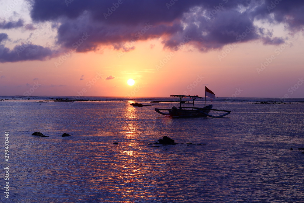 Last rays of tropical sun with fishing boat in Kuta, Bali, Indonesia