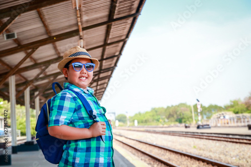 The boy wears a hat, wear blue glasses, wait for the train to travel.