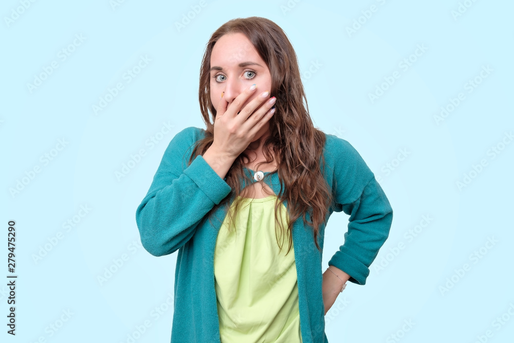Funny woman is shocked with news covering her mouth in panic. Studio shot on blue background. Funny woman is shocked with news covering her mouth in panic. Studio shot on blue background.