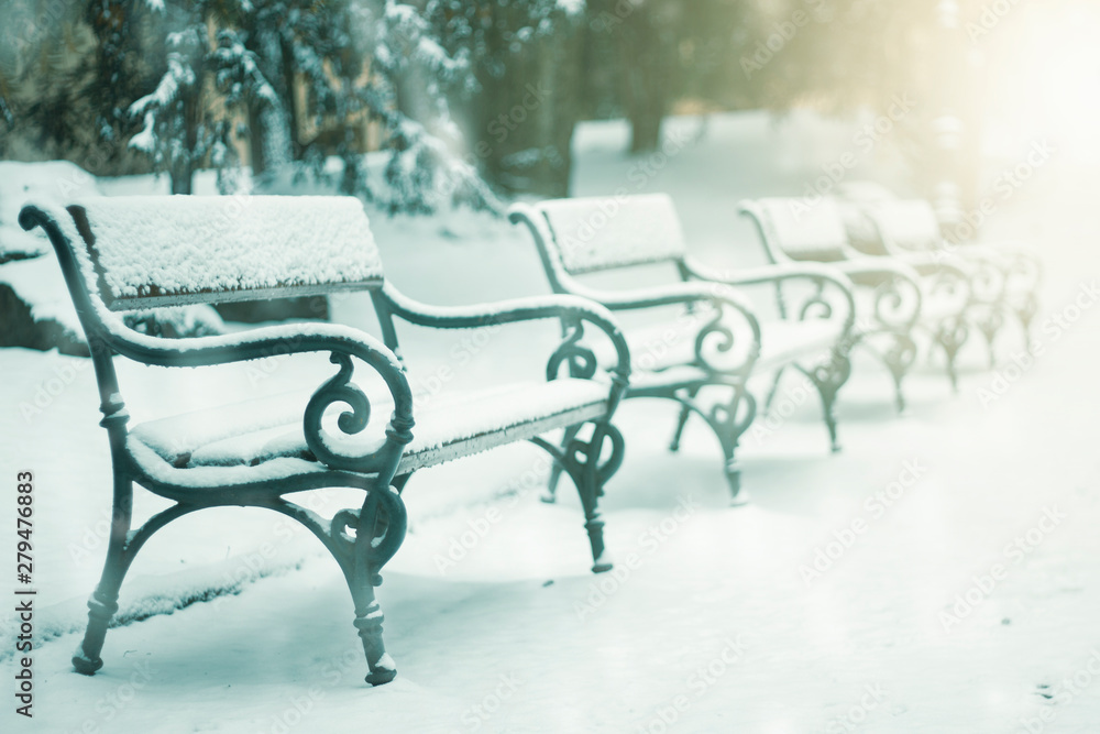 Bench in a park covered by snow and snowing flakes