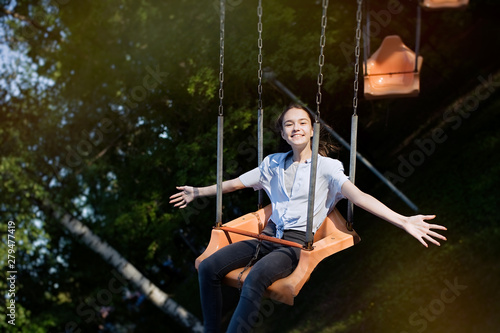 Happy child teenage girl riding chain carousel swing at amusement park 