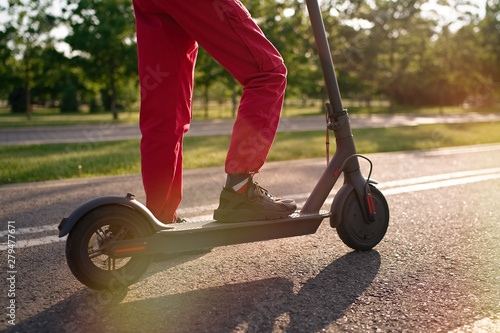 Close up of teen riding electric kick scooter in the park at sunset 