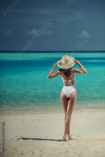 Young sexy woman on white sand beach with turquoise sea, luxury resort in the Maldives