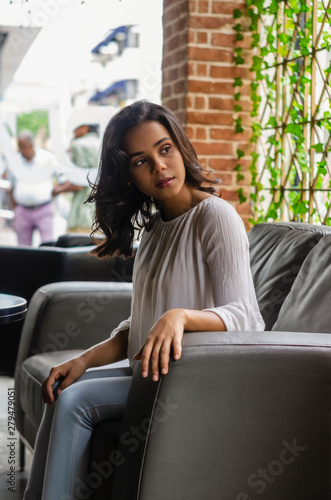 young girl from 19 to 25 years old sitting on black sofa in restaurant looking out the window waiting for her partner