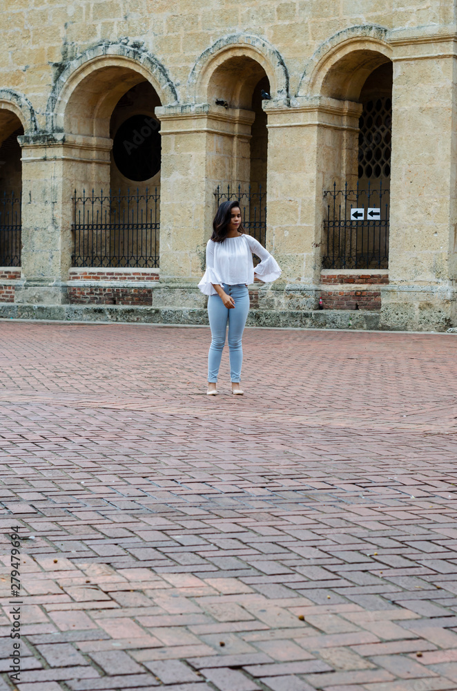 Outdoor portrait of young beautiful girl 9 to 25 years old posing in street. wearing white blouse and tight jeans and sapatillas. City lifestyle. Female fashion concept.