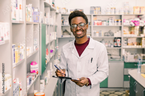 Smiling African American man pharmacist or Chemist Writing On Clipboard While standing in interior of pharmacy photo