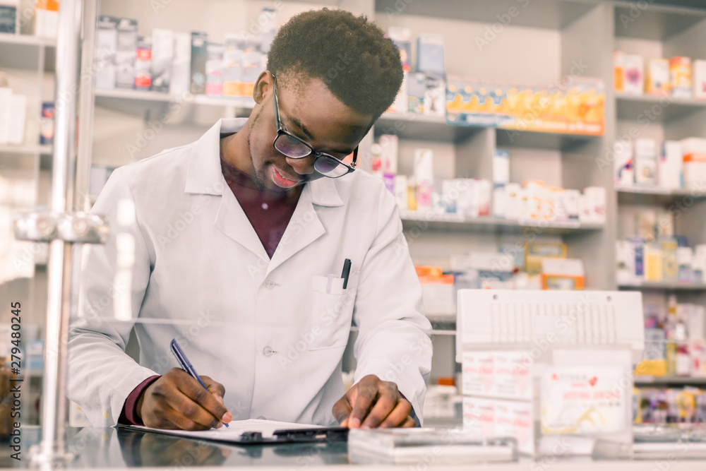 Portrait of a happy African American pharmacist writing prescription at workplace in modern pharmacy