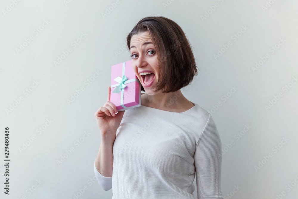 Young positive woman holding small pink gift box isolated on white background. Preparation for holiday. Girl looking happy and excited. Christmas birthday valentine celebration present concept Young positive woman holding small pink gift box isolated on white background. Preparation for holiday. Girl looking happy and excited. Christmas birthday valentine celebration present concept