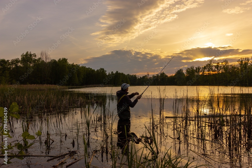 Angler catching the fish during cloudy sunset Angler catching the fish during cloudy sunset