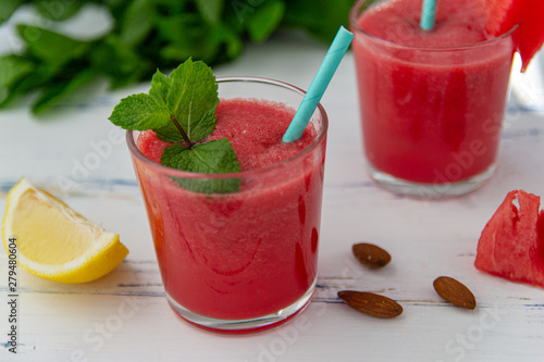 Cold watermelon smoothie with mint and lemon in glasses . Colorful refreshing drink for the summer, on a light blue background with wooden banner.