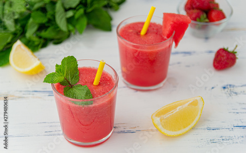 Cold watermelon smoothie with mint, lemon and strawberries in glasses . Colorful refreshing drinks for summer, on wooden light blue background.