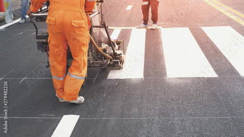 Road workers with thermoplastic spray road marking machine working to paint pedestrian crosswalk on asphalt road surface in the city