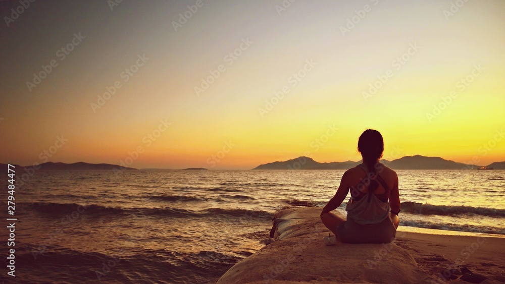 Woman meditates - relaxes at sunset by the sea on the beach. Concept for yoga, health and spa.