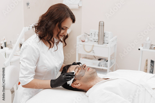 Beautician applying cosmetic mask on man's face in spa salon.