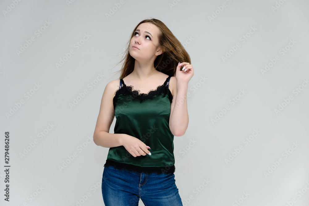 Concept portrait above the knee of a pretty girl, young woman with long beautiful brown hair in a green T-shirt and blue jeans on a white background. In the studio in different poses showing emotions. Concept portrait above the knee of a pretty girl, young woman with long beautiful brown hair in a green T-shirt and blue jeans on a white background. In the studio in different poses showing emotions.