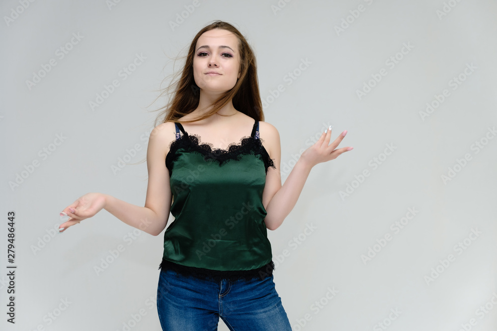 Concept portrait above the knee of a pretty girl, young woman with long beautiful brown hair in a green T-shirt and blue jeans on a white background. In the studio in different poses showing emotions. Concept portrait above the knee of a pretty girl, young woman with long beautiful brown hair in a green T-shirt and blue jeans on a white background. In the studio in different poses showing emotions.