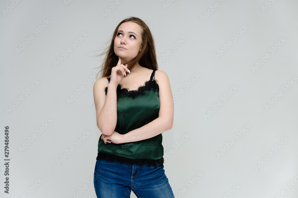 Concept portrait above the knee of a pretty girl, young woman with long beautiful brown hair in a green T-shirt and blue jeans on a white background. In the studio in different poses showing emotions. Concept portrait above the knee of a pretty girl, young woman with long beautiful brown hair in a green T-shirt and blue jeans on a white background. In the studio in different poses showing emotions.