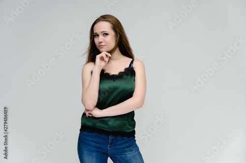 Concept portrait above the knee of a pretty girl, young woman with long beautiful brown hair in a green T-shirt and blue jeans on a white background. In the studio in different poses showing emotions. © Вячеслав Чичаев