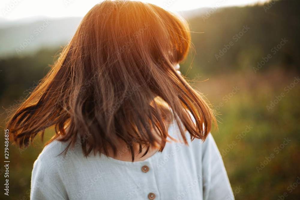 Stylish boho girl waving hair in sunny meadow at atmospheric sunset. Happy hipster woman in linen rustic dress enjoying traveling in evening mountains. Space for text Stylish boho girl waving hair in sunny meadow at atmospheric sunset. Happy hipster woman in linen rustic dress enjoying traveling in evening mountains. Space for text