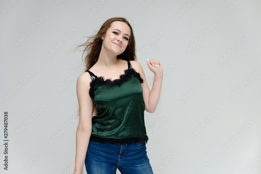 Concept portrait above the knee of a pretty girl, young woman with long beautiful brown hair in a green T-shirt and blue jeans on a white background. In the studio in different poses showing emotions. Concept portrait above the knee of a pretty girl, young woman with long beautiful brown hair in a green T-shirt and blue jeans on a white background. In the studio in different poses showing emotions.