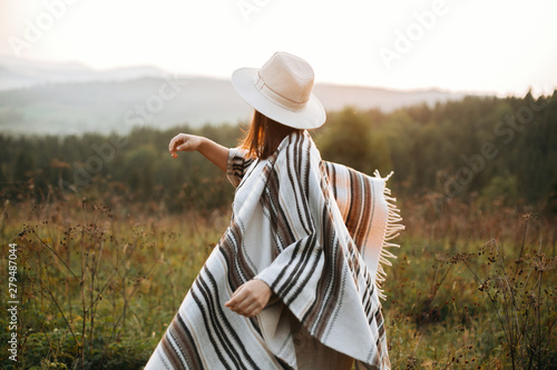 Murais de parede Stylish boho girl walking in sunny light at atmospheric sunset in meadow