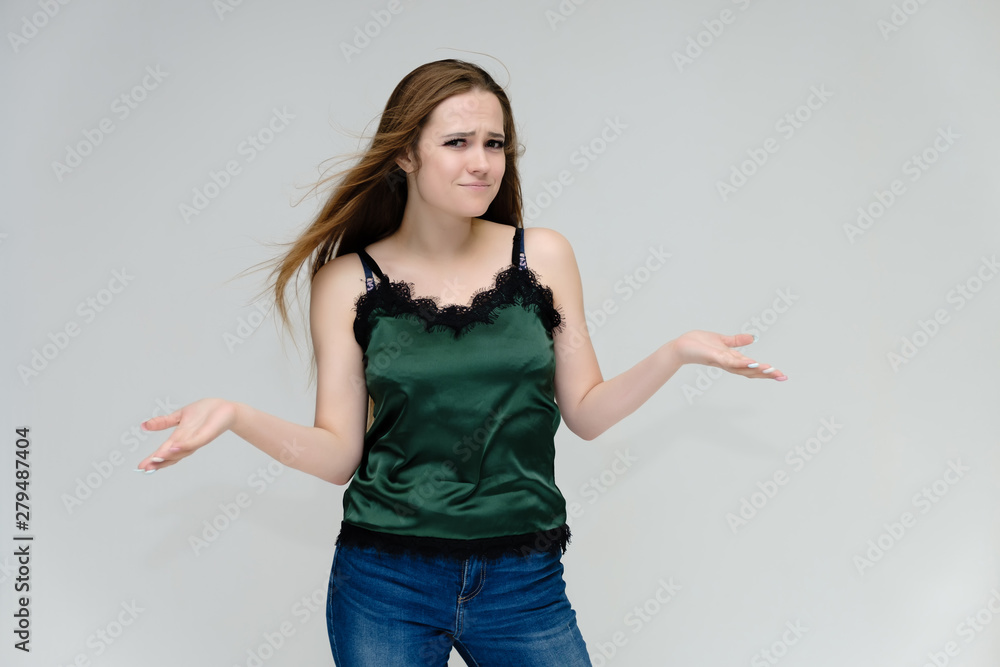 Concept portrait above the knee of a pretty girl, young woman with long beautiful brown hair in a green T-shirt and blue jeans on a white background. In the studio in different poses showing emotions. Concept portrait above the knee of a pretty girl, young woman with long beautiful brown hair in a green T-shirt and blue jeans on a white background. In the studio in different poses showing emotions.