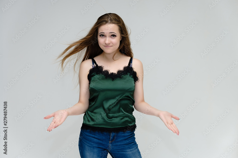 Concept portrait above the knee of a pretty girl, young woman with long beautiful brown hair in a green T-shirt and blue jeans on a white background. In the studio in different poses showing emotions. Concept portrait above the knee of a pretty girl, young woman with long beautiful brown hair in a green T-shirt and blue jeans on a white background. In the studio in different poses showing emotions.