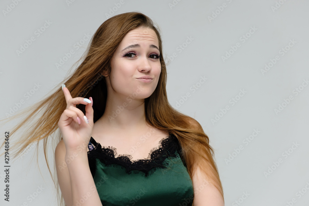 Fototapeta premium Concept close-up portrait of a pretty girl, young woman with long beautiful brown hair in a green t-shirt on a white background. In the studio in different poses showing emotions.
