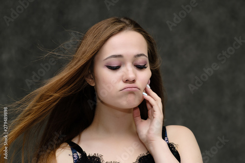 Concept close-up portrait of a pretty girl, young woman with long beautiful brown hair and beautiful face skin on a gray background. In the studio in different poses showing emotions.