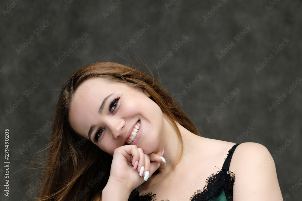 Obraz premium Concept close-up portrait of a pretty girl, young woman with long beautiful brown hair and beautiful face skin on a gray background. In the studio in different poses showing emotions.