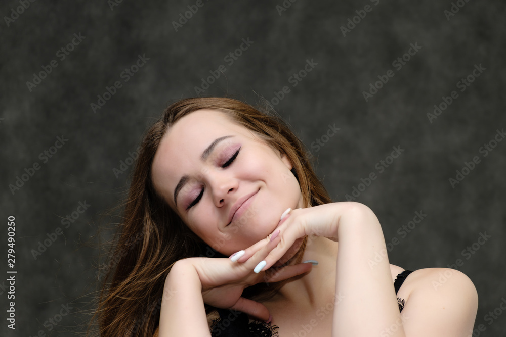 Concept close-up portrait of a pretty girl, young woman with long beautiful brown hair and beautiful face skin on a gray background. In the studio in different poses showing emotions. Concept close-up portrait of a pretty girl, young woman with long beautiful brown hair and beautiful face skin on a gray background. In the studio in different poses showing emotions.