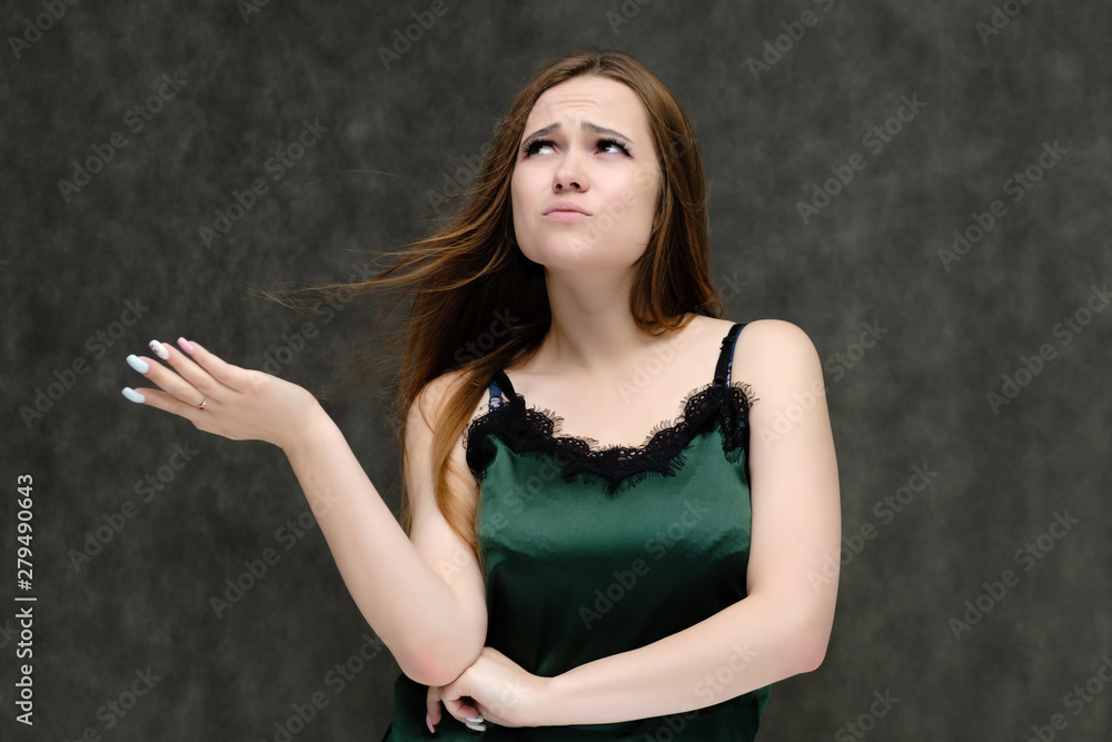 Concept portrait of the waist of a pretty girl, a young woman with long beautiful brown hair and a green T-shirt on a gray background. In the studio in different poses showing emotions. Concept portrait of the waist of a pretty girl, a young woman with long beautiful brown hair and a green T-shirt on a gray background. In the studio in different poses showing emotions.