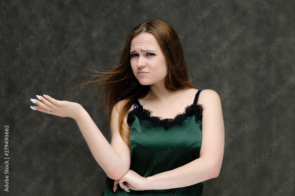 Fototapeta premium Concept portrait of the waist of a pretty girl, a young woman with long beautiful brown hair and a green T-shirt on a gray background. In the studio in different poses showing emotions.