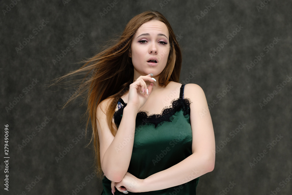 Concept portrait of the waist of a pretty girl, a young woman with long beautiful brown hair and a green T-shirt on a gray background. In the studio in different poses showing emotions. Concept portrait of the waist of a pretty girl, a young woman with long beautiful brown hair and a green T-shirt on a gray background. In the studio in different poses showing emotions.