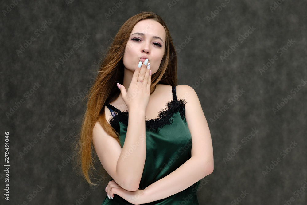 Fototapeta premium Concept portrait of the waist of a pretty girl, a young woman with long beautiful brown hair and a green T-shirt on a gray background. In the studio in different poses showing emotions.