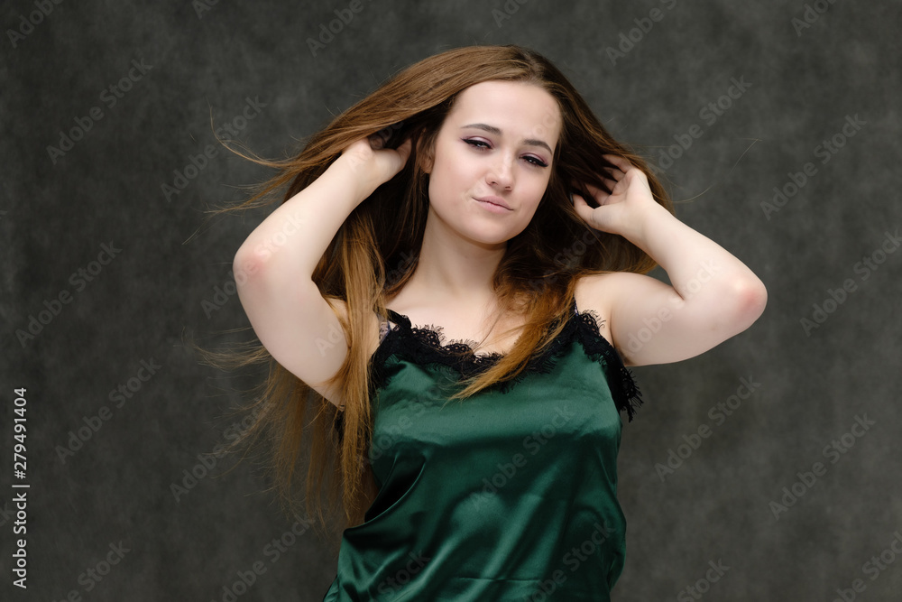 Concept portrait of the waist of a pretty girl, a young woman with long beautiful brown hair and a green T-shirt on a gray background. In the studio in different poses showing emotions. Concept portrait of the waist of a pretty girl, a young woman with long beautiful brown hair and a green T-shirt on a gray background. In the studio in different poses showing emotions.
