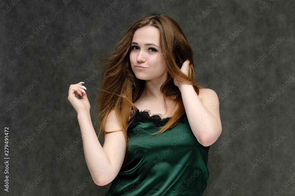Concept portrait of the waist of a pretty girl, a young woman with long beautiful brown hair and a green T-shirt on a gray background. In the studio in different poses showing emotions. Concept portrait of the waist of a pretty girl, a young woman with long beautiful brown hair and a green T-shirt on a gray background. In the studio in different poses showing emotions.