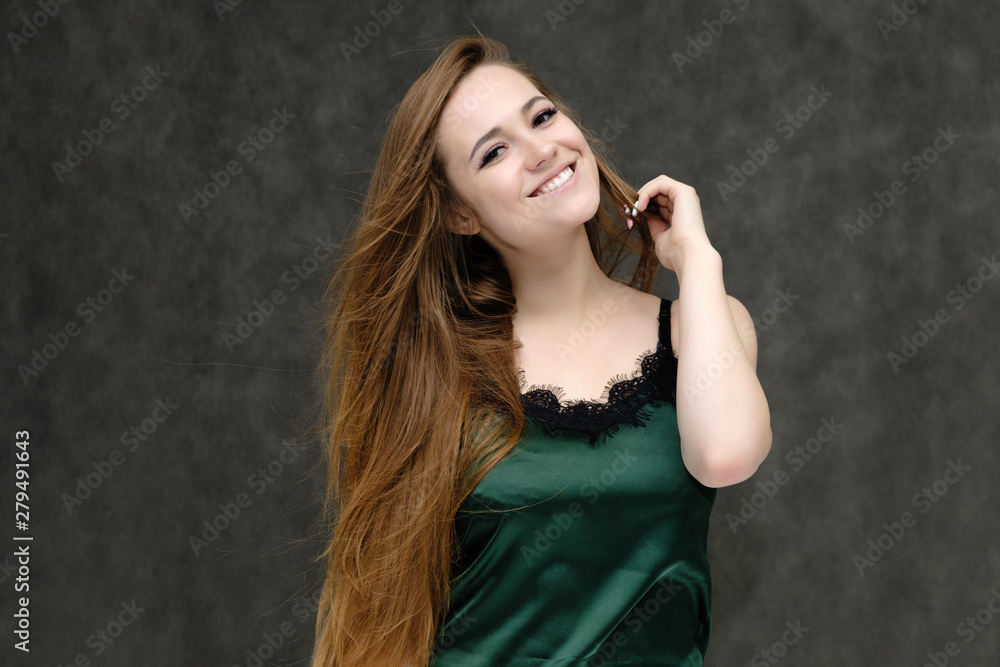 Concept portrait of the waist of a pretty girl, a young woman with long beautiful brown hair and a green T-shirt on a gray background. In the studio in different poses showing emotions.