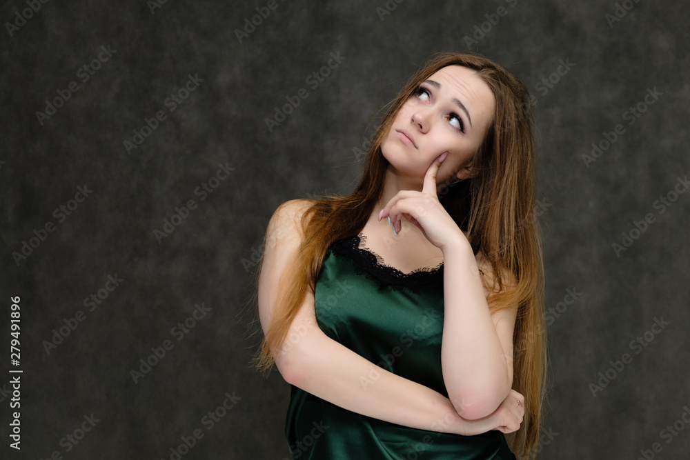 Concept portrait of the waist of a pretty girl, a young woman with long beautiful brown hair and a green T-shirt on a gray background. In the studio in different poses showing emotions. Concept portrait of the waist of a pretty girl, a young woman with long beautiful brown hair and a green T-shirt on a gray background. In the studio in different poses showing emotions.