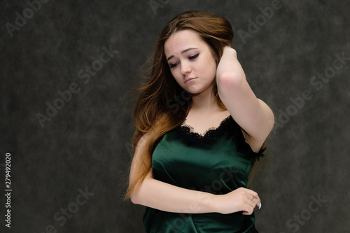 Concept portrait of the waist of a pretty girl, a young woman with long beautiful brown hair and a green T-shirt on a gray background. In the studio in different poses showing emotions.